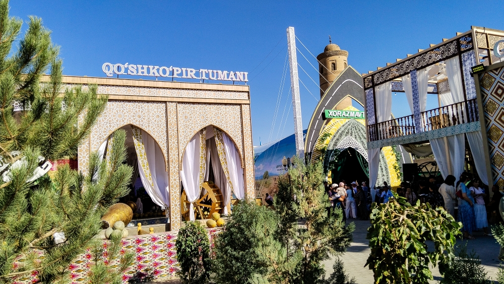 Фото — павильон «Qo'shko'pir tumani» с белой резной аркой и водяным колесом